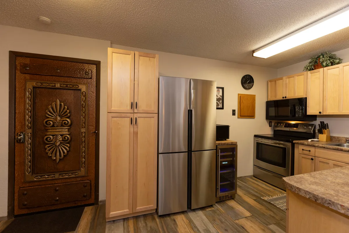 A view of a kitchen space with an ornate wooden door, stainless steel appliances, and granite countertops. The open layout allows for easy movement between spaces, and the scene suggests guests are able to cook, entertain, and socialize seamlessly.