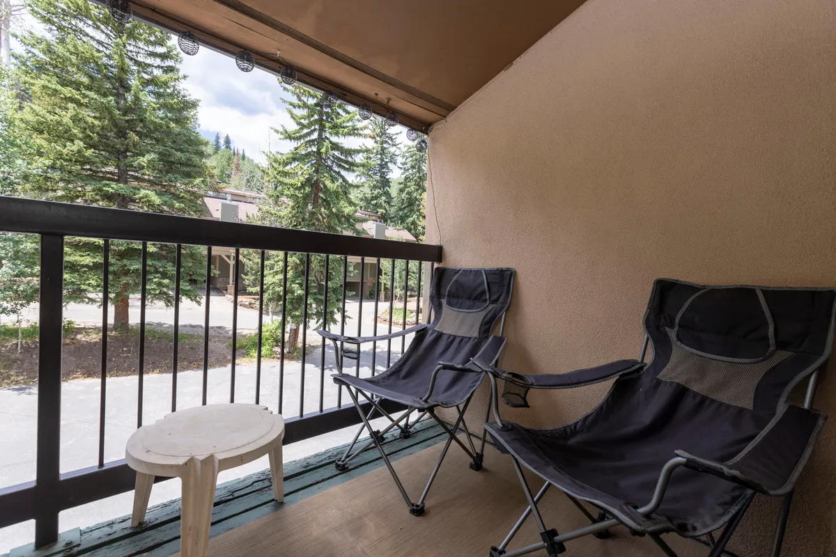 An inviting outdoor seating area with two folding chairs and a small wooden table, overlooking a serene view of trees. The setting is peaceful, perfect for relaxing with a morning coffee or unwinding after a day of adventure.