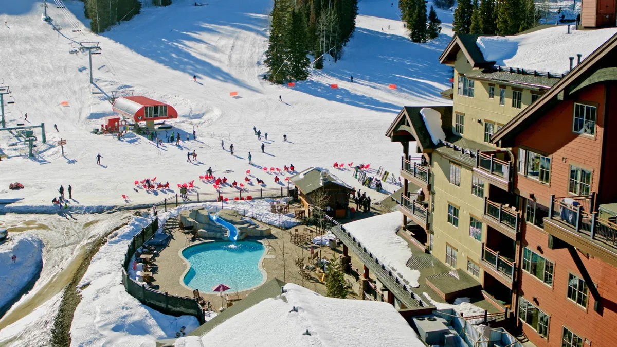 A panoramic view featuring ski slopes, an outdoor pool, skiers, snowboarders, and the lodge itself. The vibrant scene is filled with activity and energy, highlighting both the recreational opportunities and the pool area as part of the resort experience.