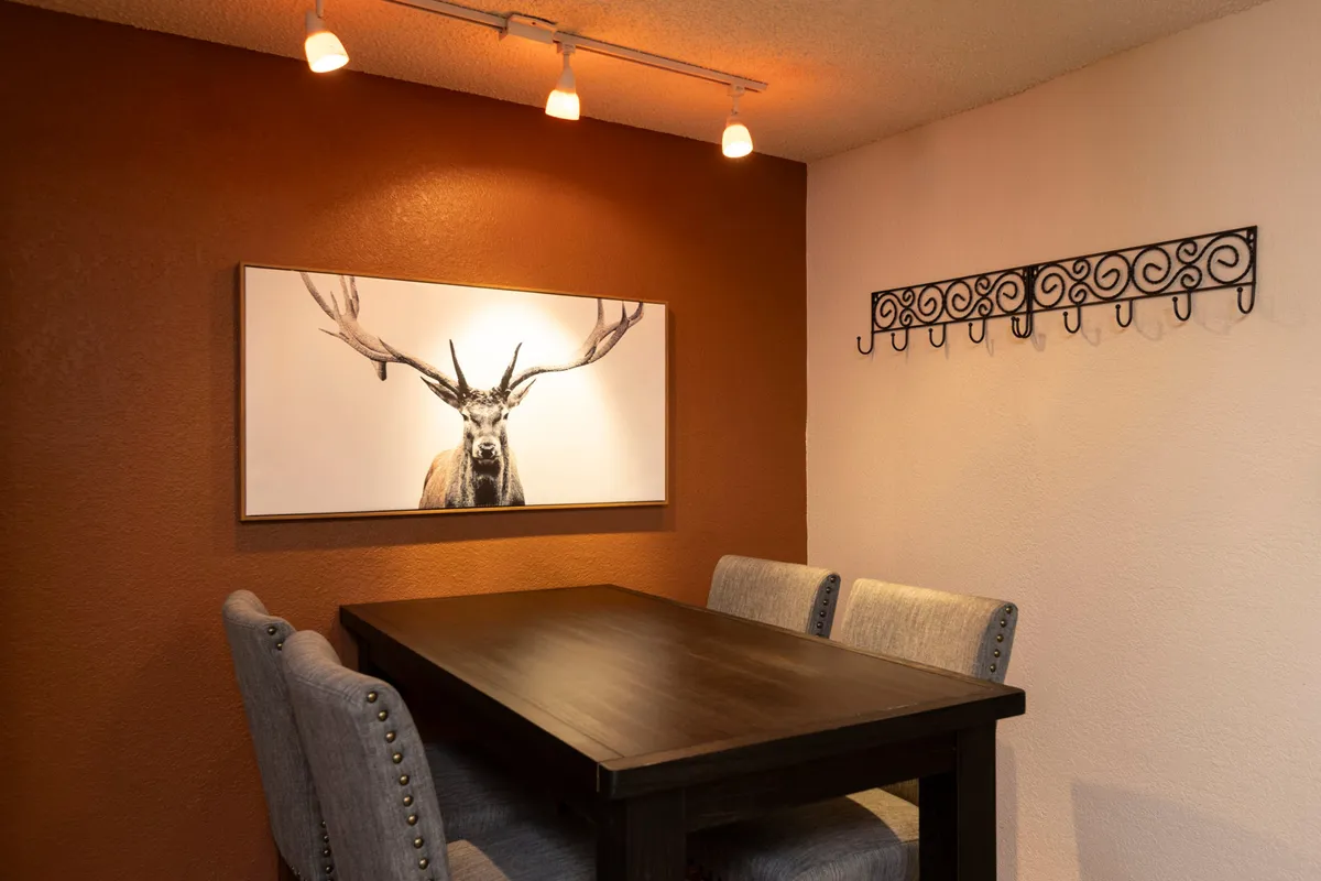 A dining area featuring a large dining table, comfortable seating, and rustic artwork, including a striking deer image. The space is softly lit, fostering a cozy environment for sharing meals and conversation after a day on the slopes.