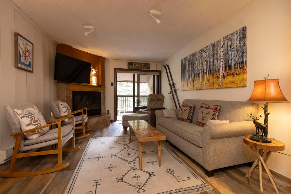 The image showcases a warm and inviting living area, centered around a crackling fireplace. A plush sofa and cozy rocking chairs are arranged for comfort, with tasteful artwork adding a homey touch. The room exudes a relaxed and sociable atmosphere, perfect for unwinding after a day of mountain adventures.