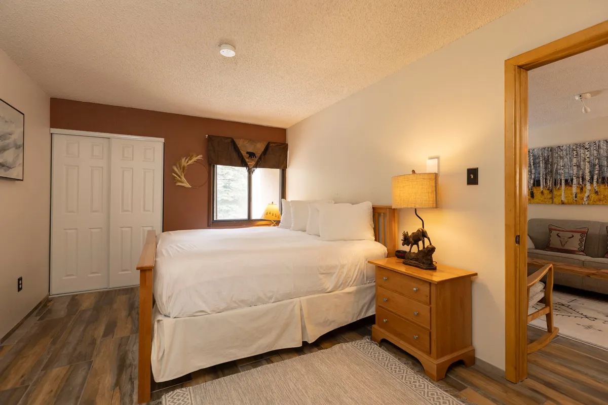 A bright, inviting bedroom featuring a plush king-sized bed adorned with soft bedding. Natural light streams in from a large window, creating a soothing atmosphere perfect for relaxation. Warm lighting from a bedside lamp and soft decor accents further enhance the tranquil feel, making this space ideal for restful nights for parents or couples.