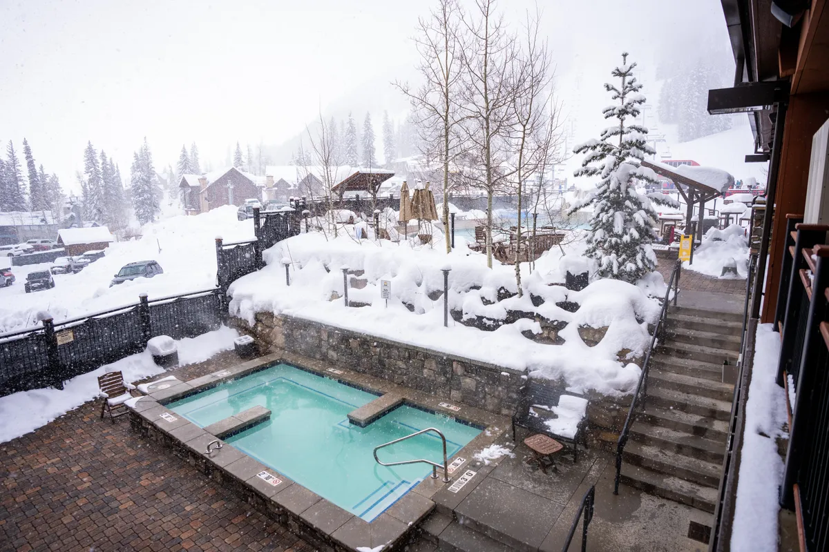 An inviting outdoor hot tub steams against a backdrop of snow-covered trees and landscape. Steps lead up to the tub, suggesting easy access, and the scene highlights the unique experience of soaking in warmth while surrounded by winter beauty.